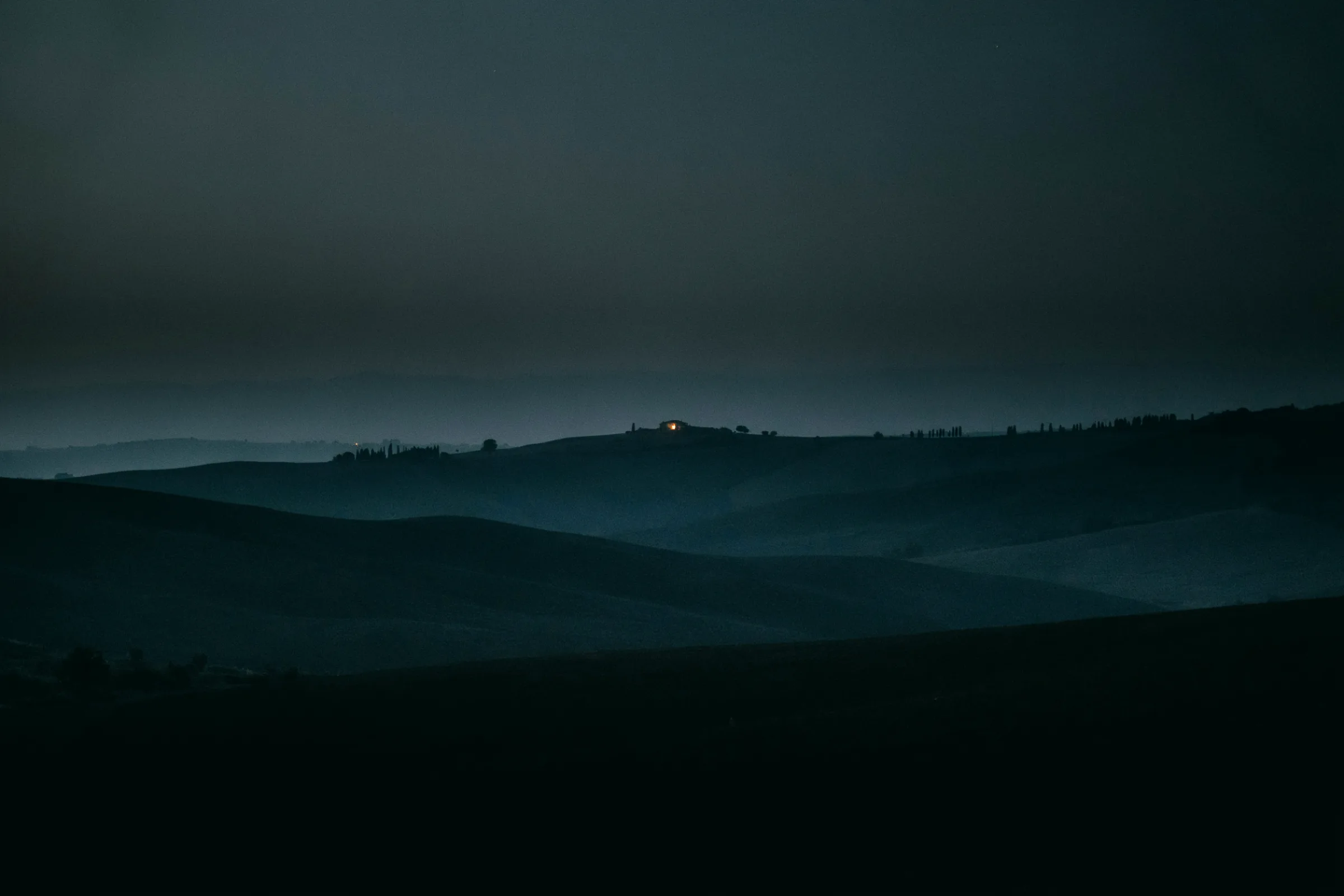 A single warm lit window in a dark house at night, everyone else asleep