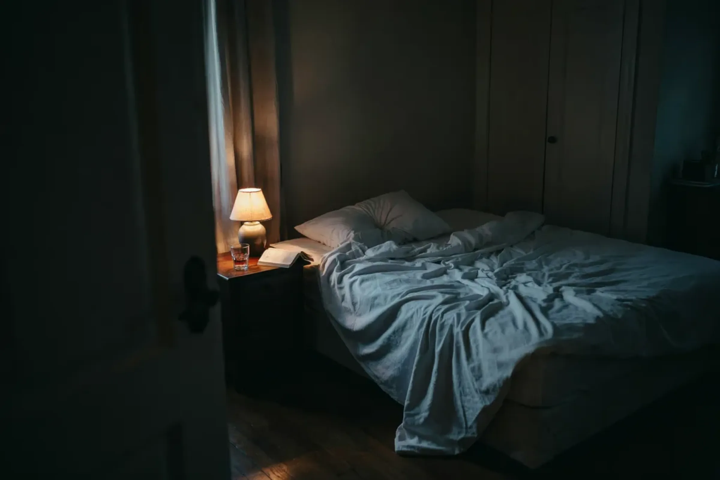 Rumpled bedsheets in a dim room, lit by one warm bedside lamp